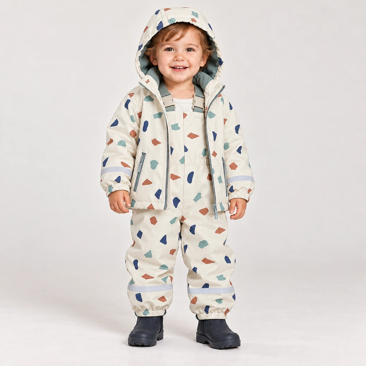 Toddler wearing HONEYKING rain jacket and bib rain pants in cream terrazzo print